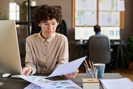 Serious businesswoman in eye glasses sitting at office desk with computer and learning about Probate